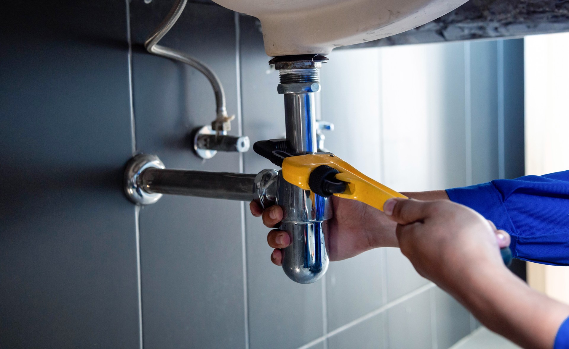 Plumber fixing white sink pipe with adjustable wrench.